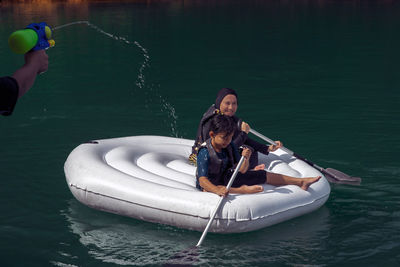 Boy spraying water on people in boat on sea