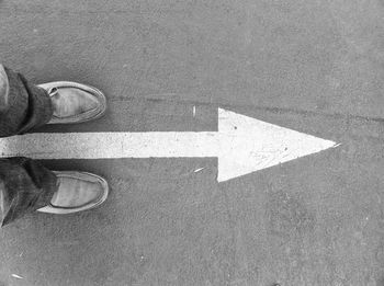 Low section of person standing on road with arrow sign