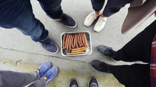 Low section of friends standing by sausages on barbecue