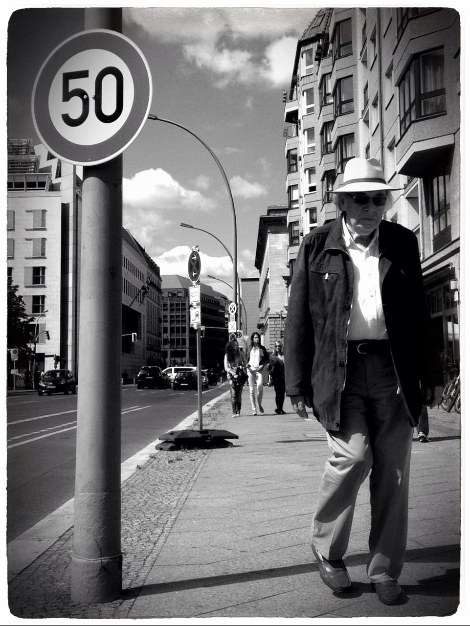 building exterior, architecture, built structure, city, men, sky, walking, street, transfer print, city life, person, lifestyles, communication, full length, road sign, cloud - sky, rear view, transportation, auto post production filter