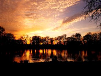 Silhouette trees by lake against orange sky