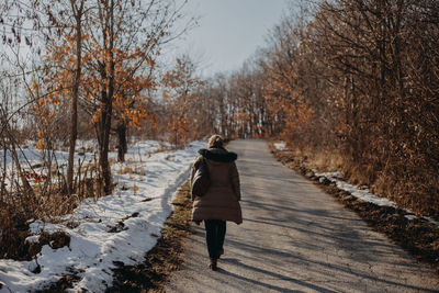 Rear view of woman walking on snow covered footpath