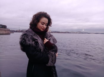 Young woman standing by river against sky during winter