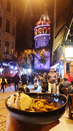 People on illuminated street amidst buildings at night