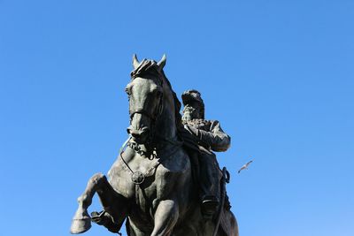 Low angle view of man and horse statute against clear blue sky