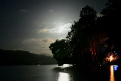 Silhouette trees by calm lake against sky