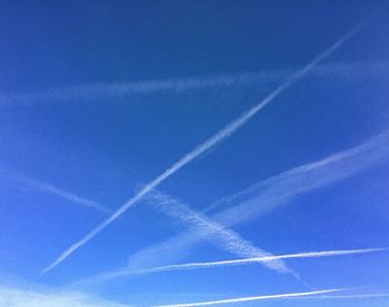 Low angle view of vapor trails against blue sky