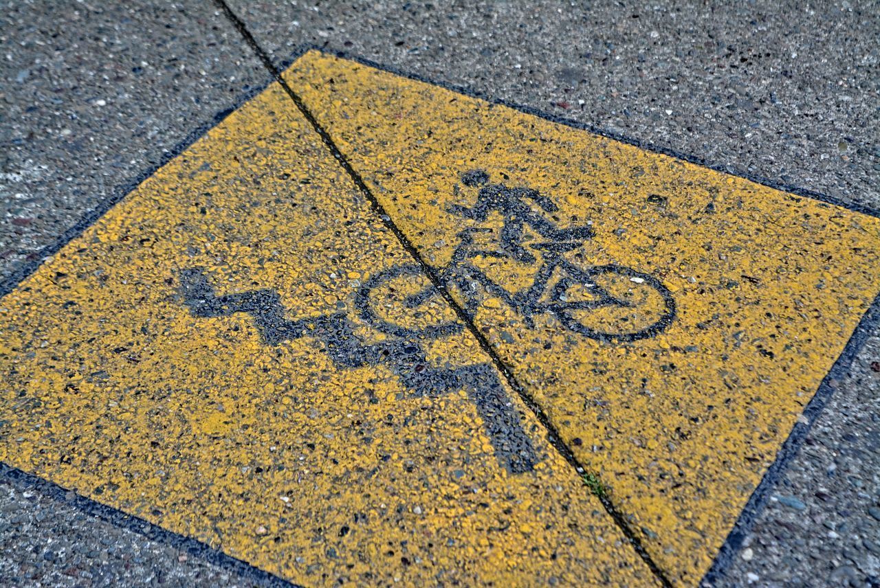 HIGH ANGLE VIEW OF YELLOW ARROW SYMBOL ON ROAD