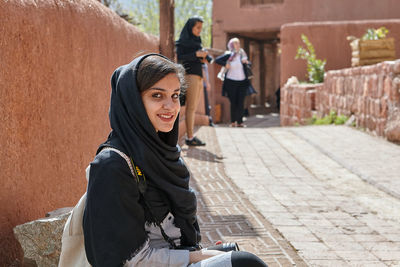 Portrait of young woman looking down while sitting on footpath