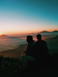 People sitting on beach against sky during sunset