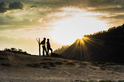 Silhouette men standing on field against sky during sunset