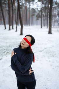 Sensual asian woman in snowy forest in winter, her eyes are tied with a red ribbon.