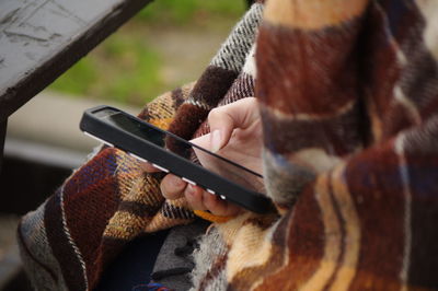 Midsection of woman with blanket using mobile phone outdoors