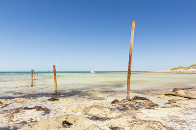 Rusting metal poles stick out of the ocean with blue sky behind