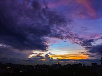 Silhouette buildings against cloudy sky at sunset