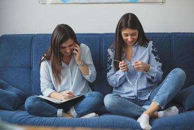 Women talk on the phone and knit in a cozy atmosphere on a blue sofa, concept hobbies and friendly