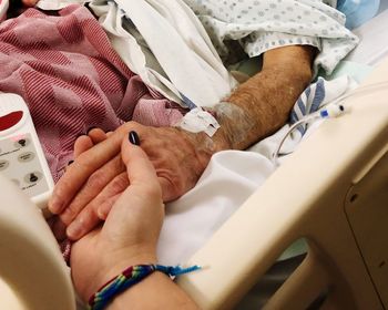 Cropped image of woman holding hands with male friend lying on bed in hospital