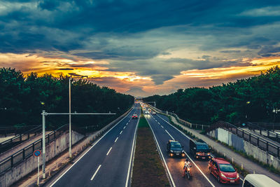 Vehicles on road against sky during sunset