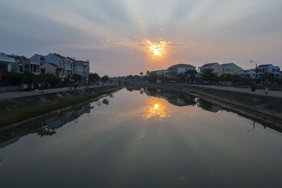 Scenic view of lake by buildings against sky during sunset