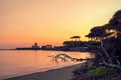 Distant view of torre astura in sea against orange sky during sunset