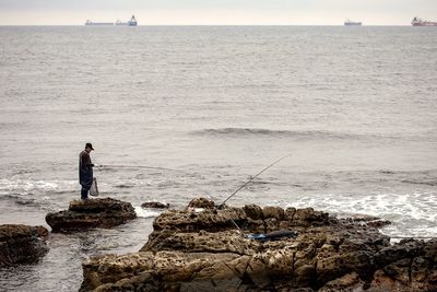 Man fishing on beach against sky