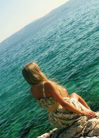 Rear view of woman sitting on rock at beach against sky