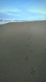 Footprints on sand at beach against sky