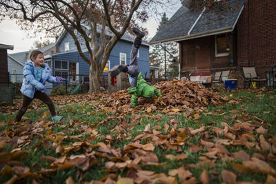 A boy cartwheels into a leaf pile while his happy sister runs around