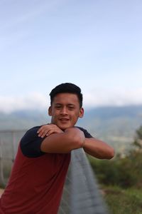 Portrait of smiling young man standing at railing against sky