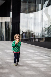 Full length of girl eating food while standing against building in city