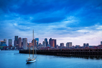 Sailboats in river by buildings in city against sky