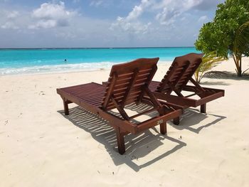 Empty chairs on beach against sky