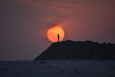 Silhouette people on rock by sea against sky during sunset