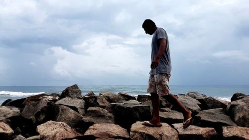 Rear view of man standing on rock by sea against sky