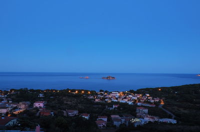 High angle view of townscape by sea against clear blue sky