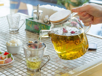 Close-up of hand pouring tea in glass on table