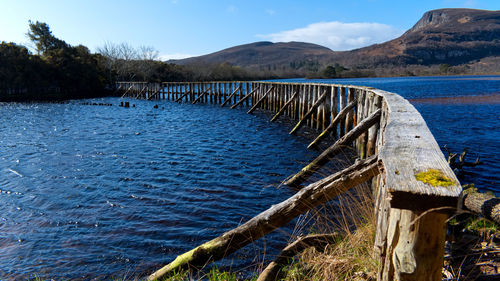 Wooden posts in lake against blue sky