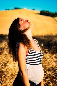 Side view of young woman standing against sky