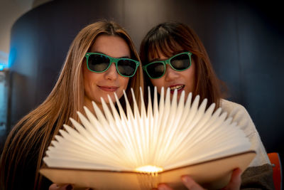 Multi-ethnic female couple of girlfriends are looking at a magical bright book indoors