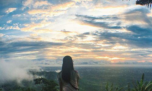 Rear view of woman sitting on landscape against sky