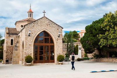 Man walking by building against sky