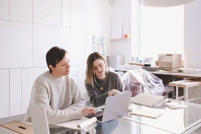 Female fashion designers discussing over laptop at desk in studio