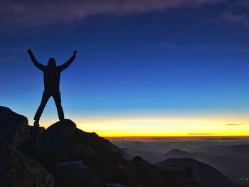 Silhouette man standing on rock against sky during sunset