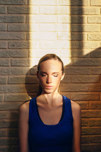 Portrait of a young woman sitting against wall