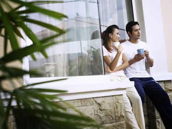Smiling couple talking while having coffee against wall