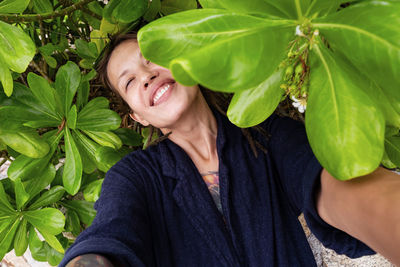 Funny smiling woman taking selfies among tropical leaves.