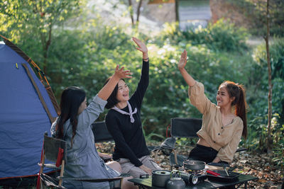 Three best friends go camping, having fun chatting and raise their hand, enjoying camping concept