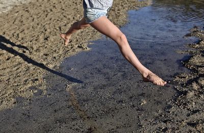 Low section of playful woman jumping over water on shore at beach