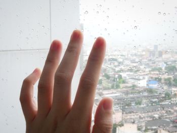 Cropped image of hand touching raindrops on glass window