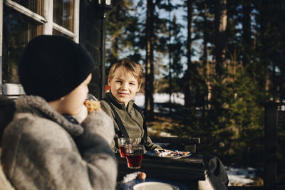 Smiling boy talking with friend while having drink at porch during winter